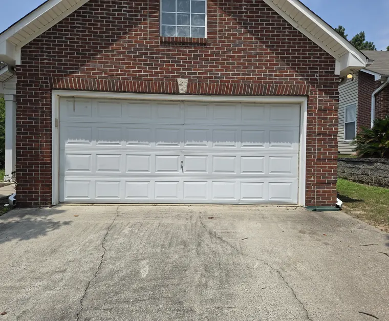 A white raised-panel double garage door on a red brick garage with a window in the gable