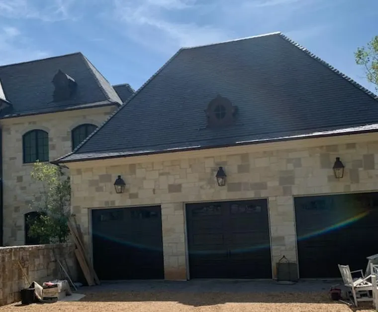 Three dark garage doors with wall lanterns on a stone house with a slate roof