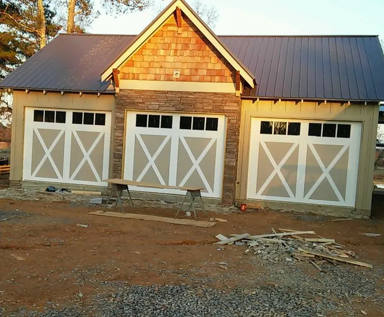 Three white garage doors with X bracing and window rows on a new cedar-shingle and stone garage