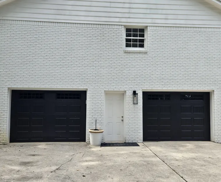 Two black carriage-style garage doors with window rows on a white-painted brick house