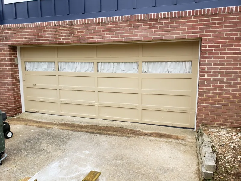 A tan garage door with covered windows before the job