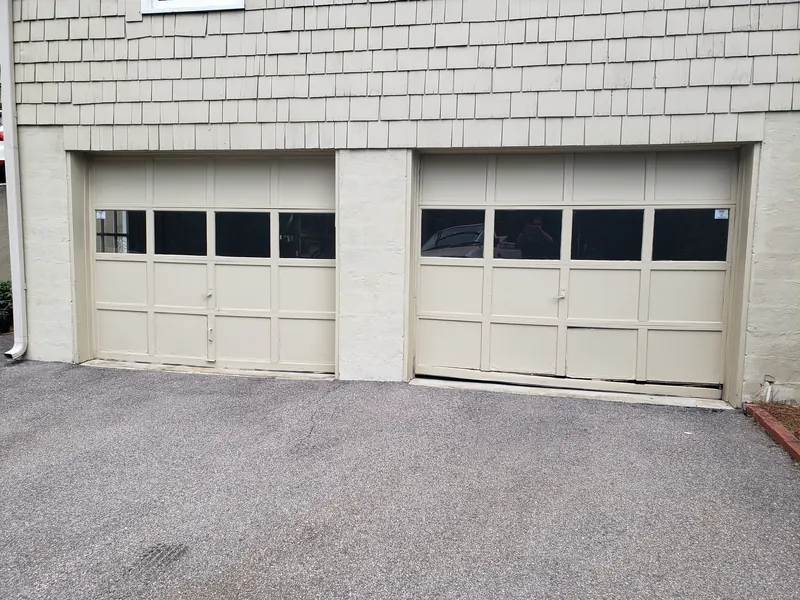 Two older tan garage doors with a row of windows
