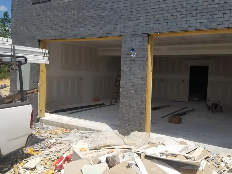 Two empty garage openings on a new dark brick house, framed but without doors