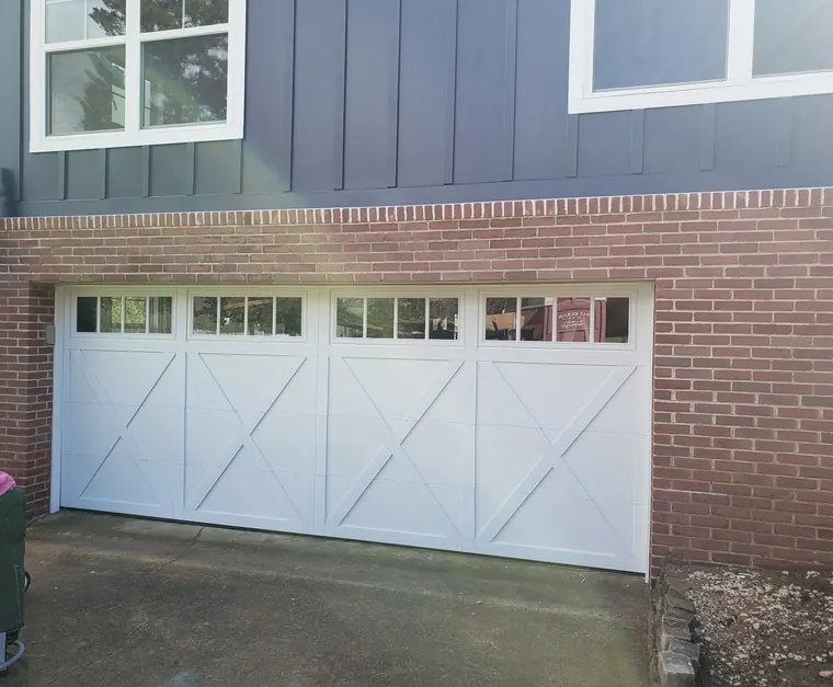 A white carriage-style garage door with X bracing and a row of windows