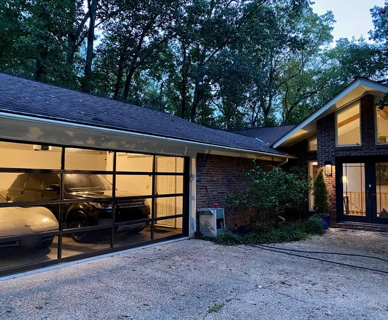 A full-view glass and black garage door glowing at dusk on a brick and wood house