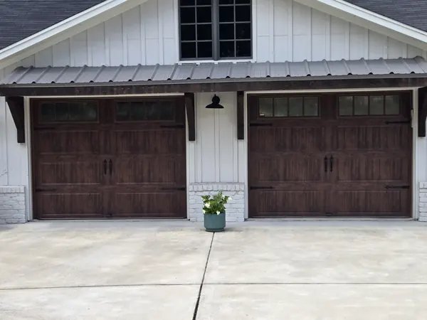 Two dark wood-look carriage doors under a metal awning on a white farmhouse
