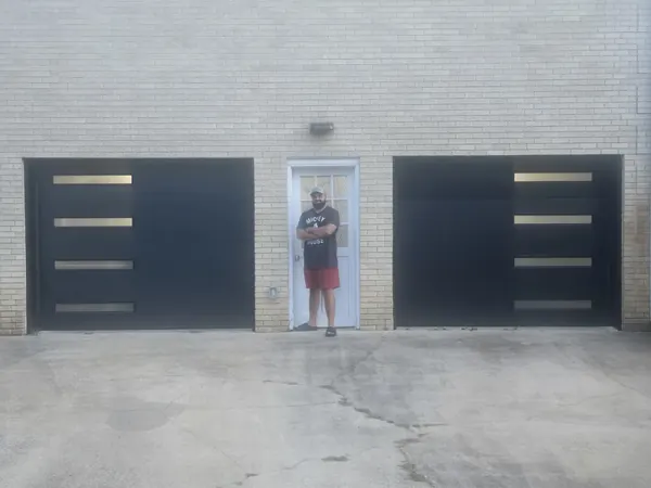 Two black modern garage doors with frosted glass strips on a white brick house