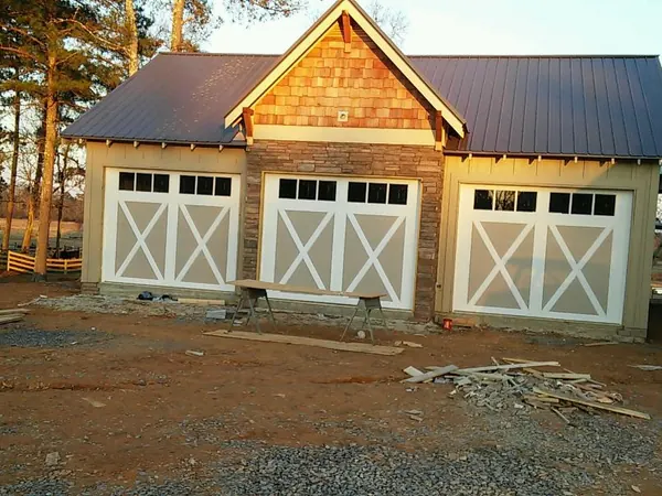 Three white garage doors with X bracing on a new cedar-shingle garage