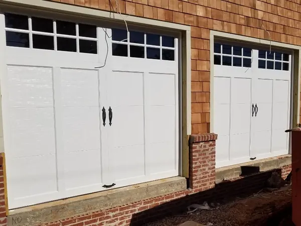 White carriage doors with windows on a cedar-shingle house under construction