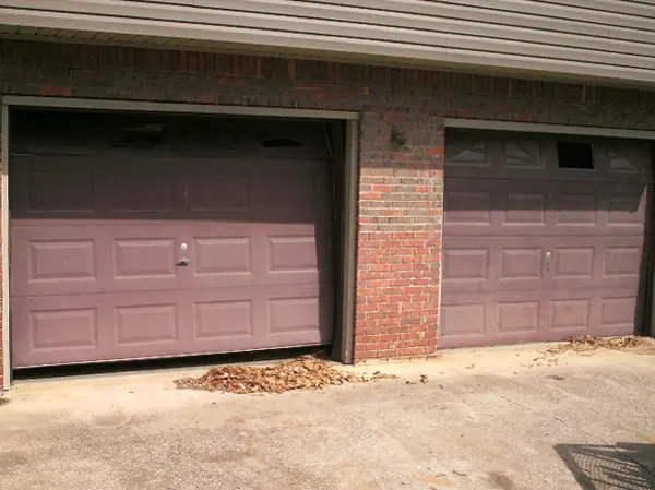 Two worn brown garage doors on a brick house